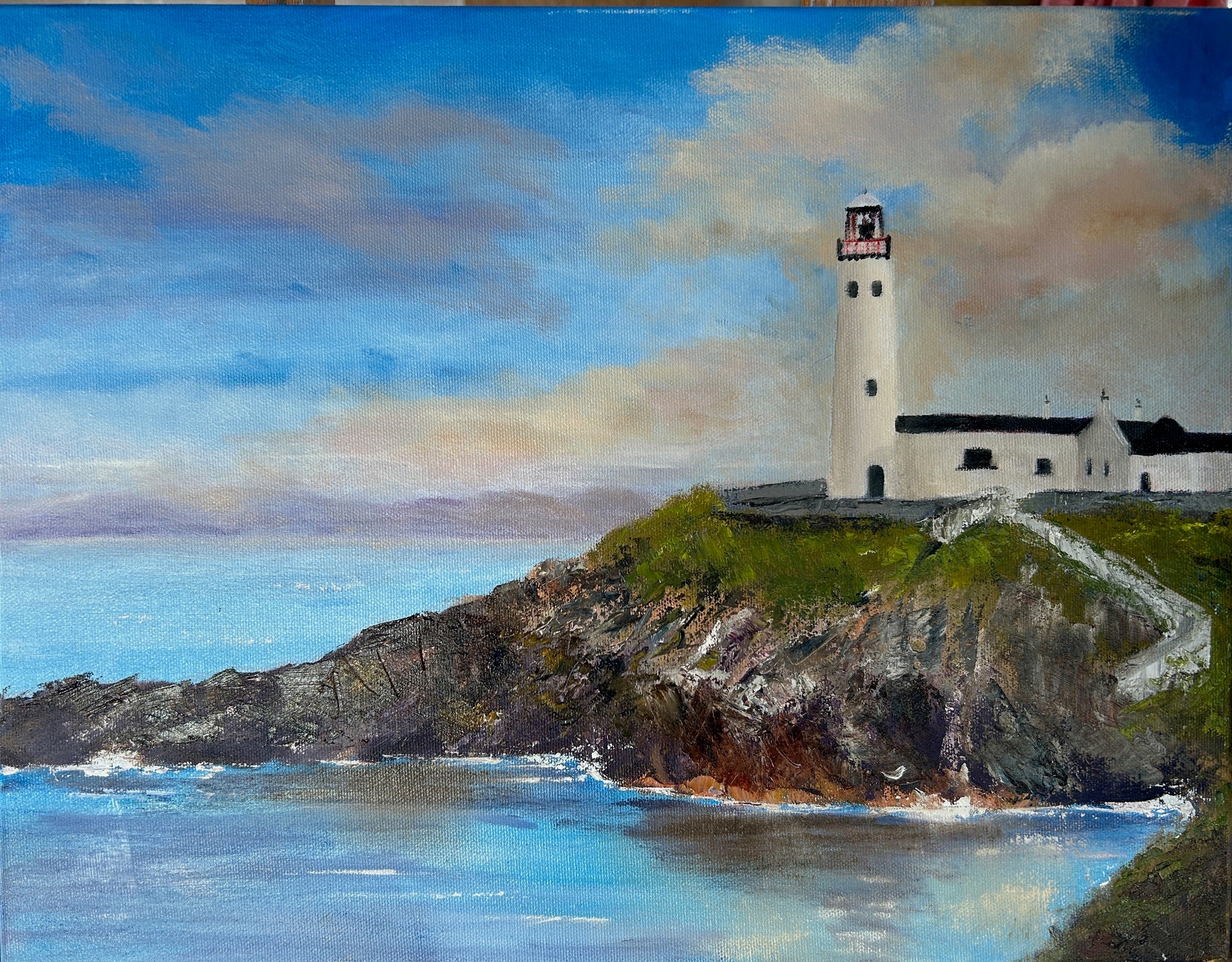 A painted coastal scene featuring a white lighthouse and small building on a rocky green cliff above blue water under a cloudy blue sky.