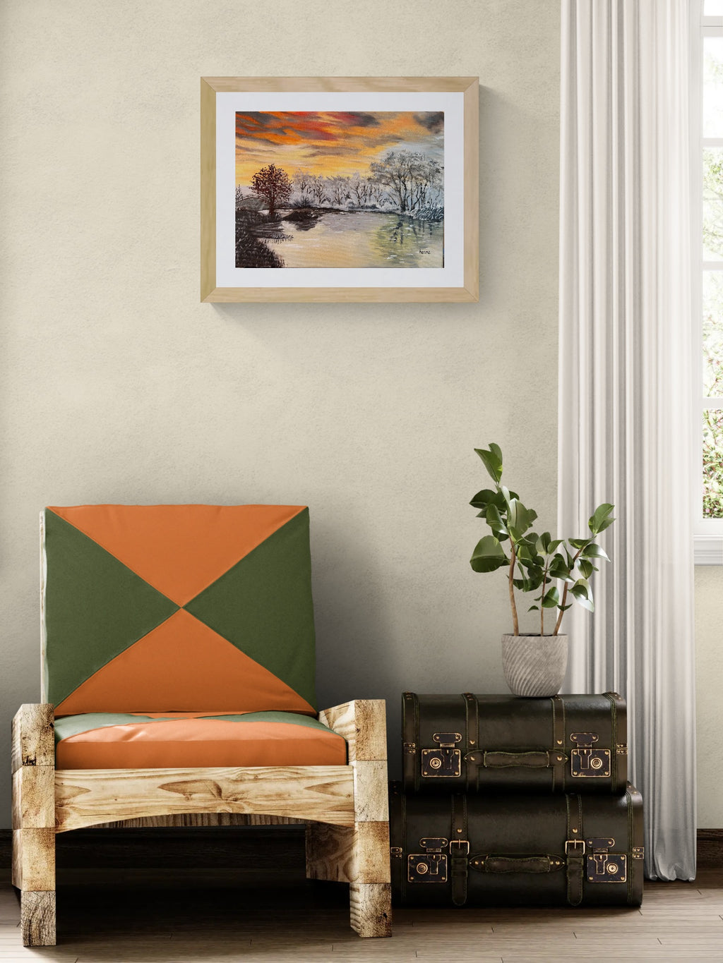 A framed landscape art print hangs on a beige wall above a rustic wooden chair with orange and green geometric cushions, next to a potted plant and stacked vintage-style trunk cases.